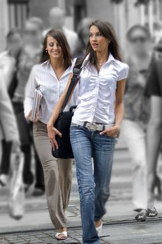 two young women between the crowd crossing the road in the center of town