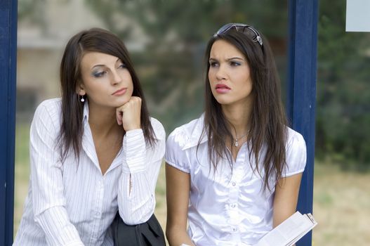 close up of two nice brunette sitting down outdoor at the bus stop