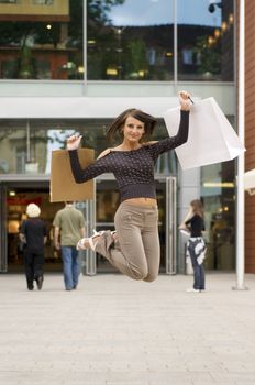 cute brunette jumping for joy in fronto of a commercial center after time for buy