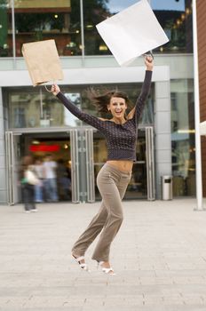 cute brunette jumping for joy in front of a commercial center after some purchases