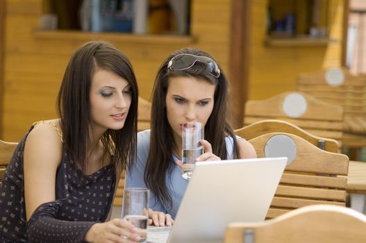 two young woman sitting in a outdoor pub looking at the computer and drinking