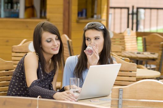 two young woman sitting in a outdoor pub working at the computer