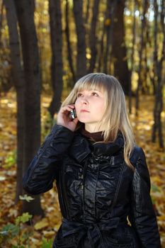 beautiful young woman talking by phone in autumn park
