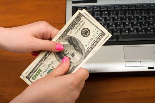 Female hands hold dollar denominations over the laptop.