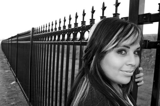 A young girl with highlighted hair posing by a fence - black and white.