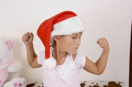 little girl wearing christmas hat and showing her muscles