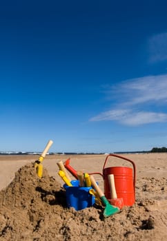 Red watering can, plastic blue bucket and other beach toys in the sandy seashore