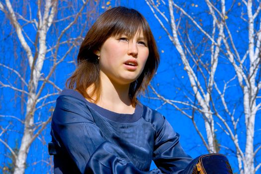 Portrait of the asian young girl against blue sky and birches