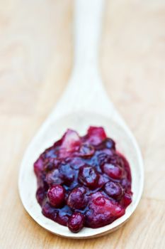 Large wooden spoon filled with homemade cranberry relish made with whole cranberries, raisins and apples. 