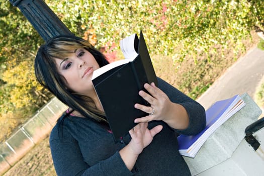 A young woman with highlighted hair reading a book or doing homework on campus.