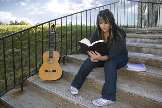 A young woman with highlighted hair reading a book or doing homework on campus.