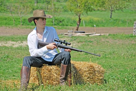 young cowboy holding a gun sitting on a hay bale