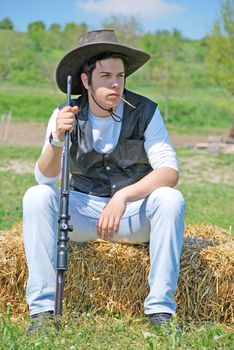 young cowboy holding a gun sitting on a hay bale