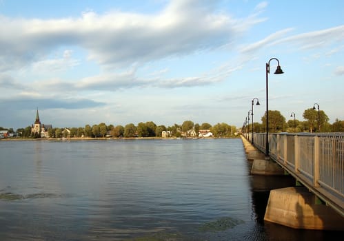 A bridge over a calm river with a view of a village