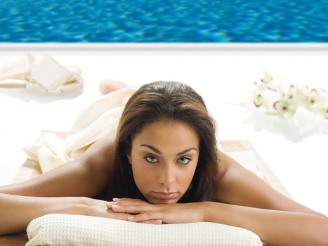 portrait of a beautiful brunette laying down on a wood carpet near a swiming pool