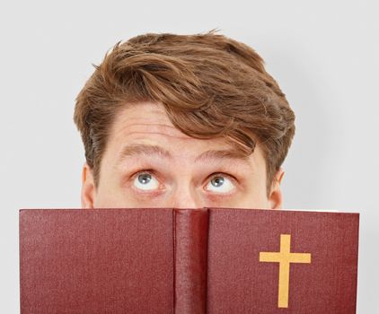 The young man thinks after bible reading on gray background