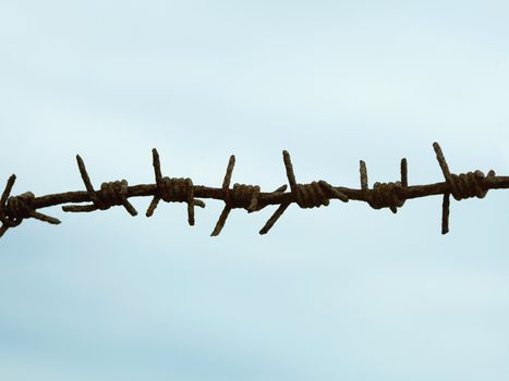 Ancient rusty barbed wire against the blue sky
