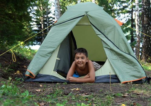 smiling boy in camping tent in forest