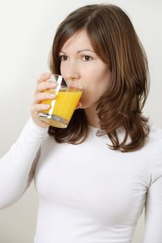 Photograph of a beautiful brunette drinking a glass of orange juice.