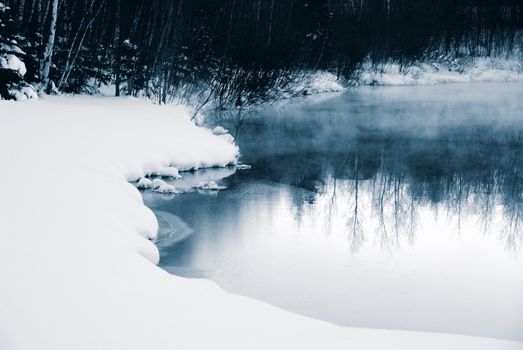 A winter landscape showing a foggy river in blue tones