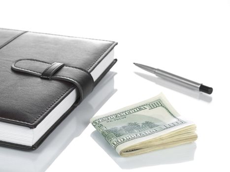 A booknote with several hundred dollar bills and a pen, isolated on white.
