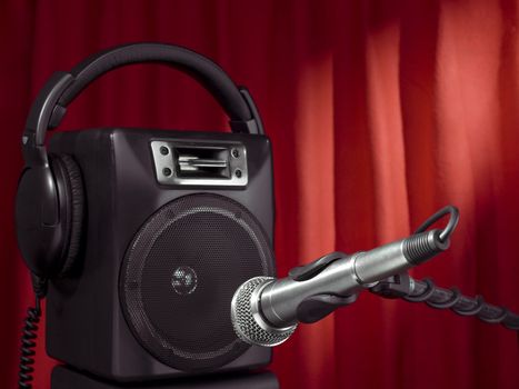 Professional microphone, headphone and speaker with a red curtain on the background.