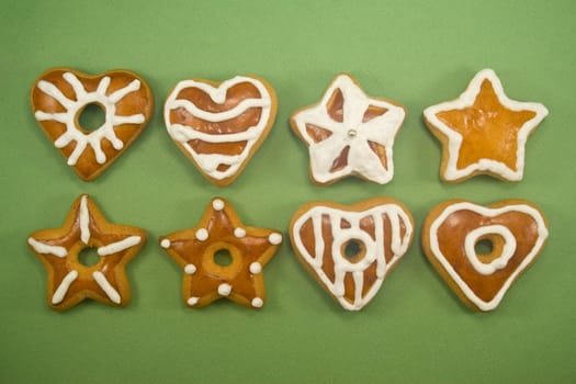 Two lines of star and heart shaped gingerbread cookies against green background