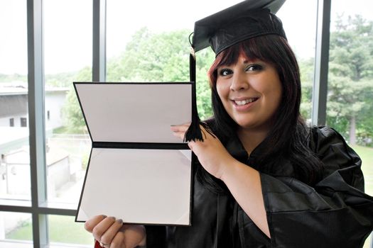 A student that recently had a school graduation posing proudly with her diploma indoors.