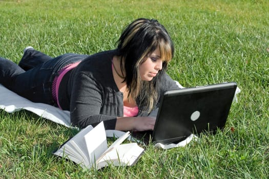 A young student using her laptop computer while laying in the grass on a nice day.