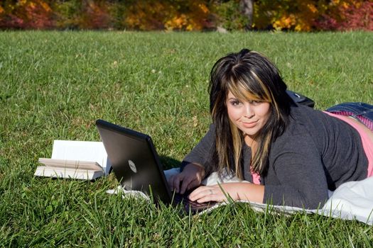 A young student using her laptop computer while laying in the grass on a nice day.