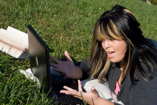 A young student using her laptop computer while laying in the grass on a nice day.