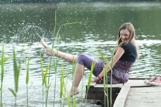 Laughing beautiful girl sitting on scaffolding near river. Her feet splashing water