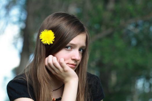 Beauty sad teen girl portrait with yellow flower in her hair on background with green forest