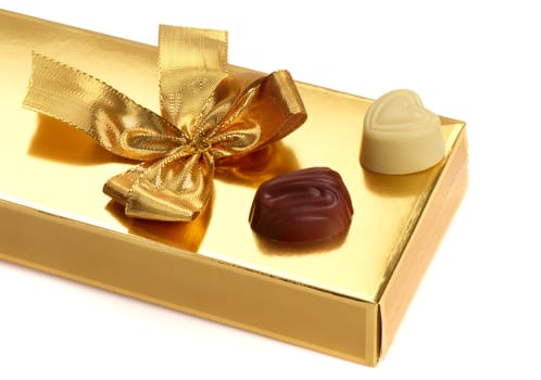 A gold boxed gift with gold ribbon and chocolate.