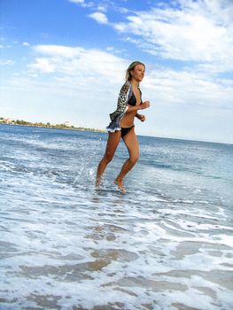 A beautiful woman running along the shore in water