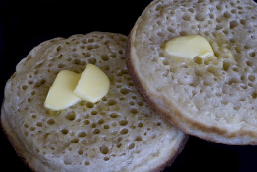 two hot crumpets with melted butter, isolated on a black backdrop