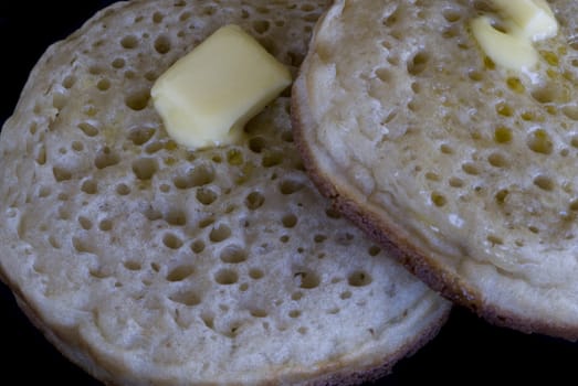two hot crumpets with melted butter, isolated on a black backdrop