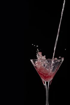 Cocktail pouring with splash from red martini isolated on black