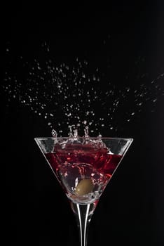 Cocktail splash with an olive on red martini with black background