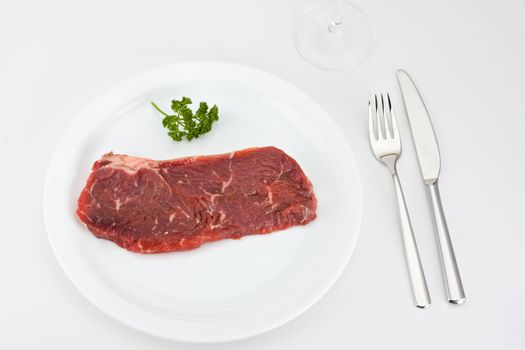 raw steak on a white plate with cutlery