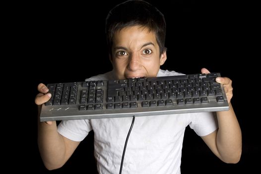 frustrated teenage boy is biting on his keyboard isolated on black