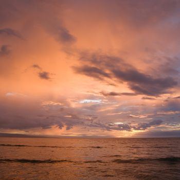 Orange glowing clouds during sunset on coast in Maui Hawaii.