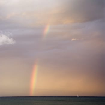 Rainbow spreading across sky on coast in Maui Hawaii.