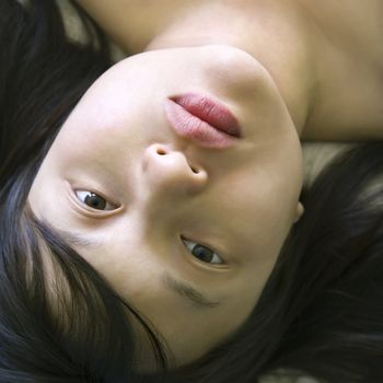 Head and shoulder portrait of pretty young Asian woman lying in bed making eye contact.