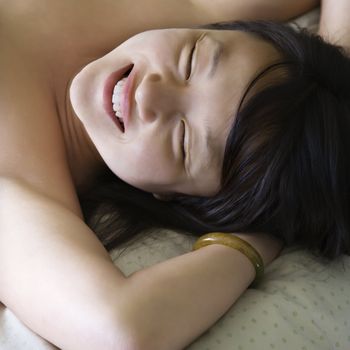 Portrait of pretty young Asian woman lying in bed smiling with eyes closed.