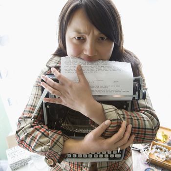 Pretty young Asian woman holding typewriter and biting page.