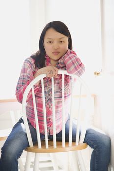 Pretty young Asian woman sitting on chair at table in kitchen.