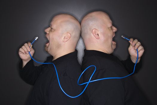 Caucasian bald mid adult identical twin men standing back to back yelling into ethernet cable.