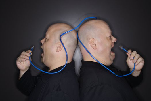 Caucasian bald mid adult identical twin men standing back to back yelling into ethernet cable.