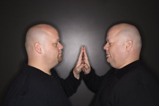 Caucasian bald mid adult identical twin men standing face to face with hands touching.